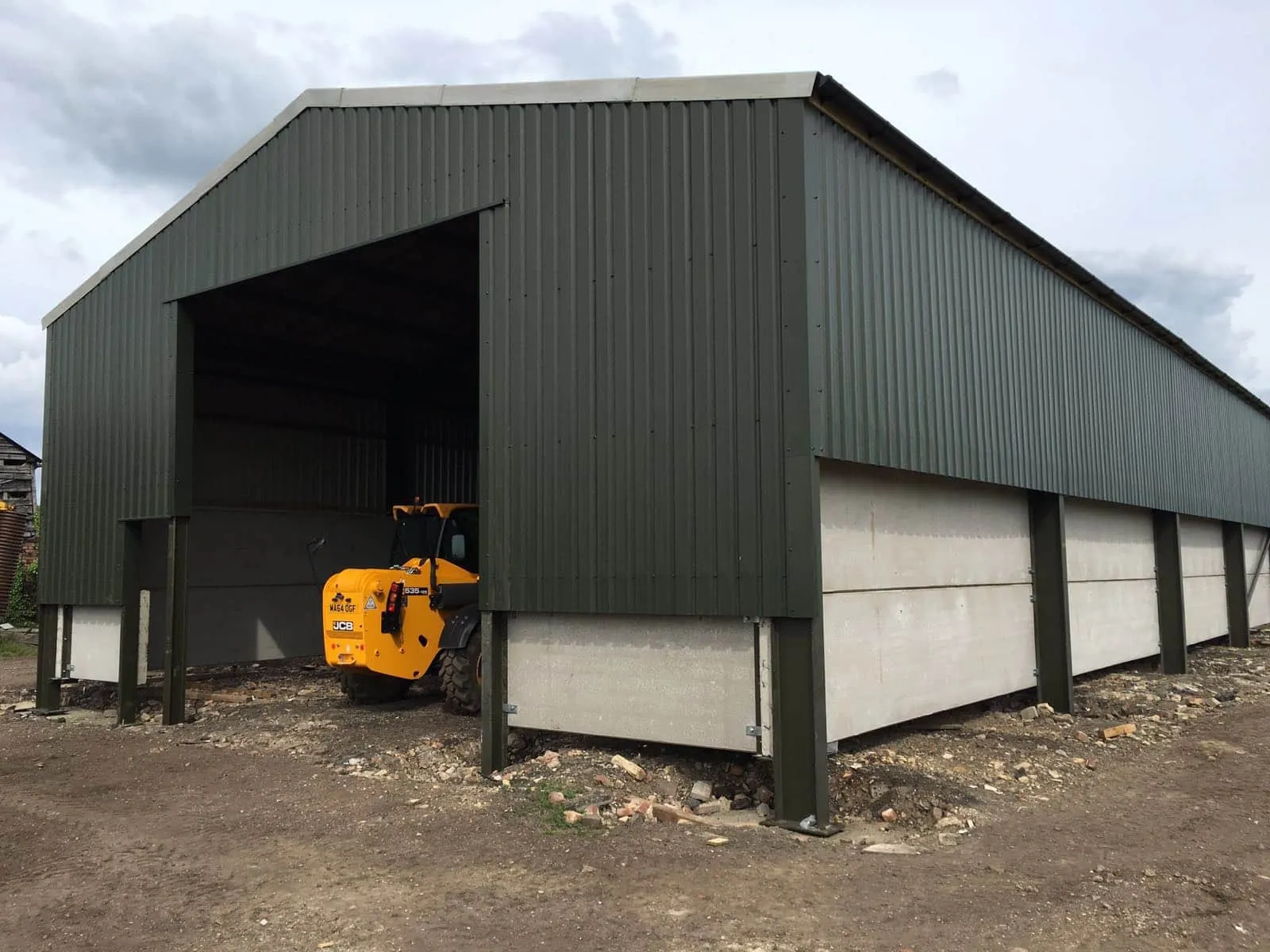 Green profiled-sheet clad barn with concrete panel base and a telehandler parked in the open bay