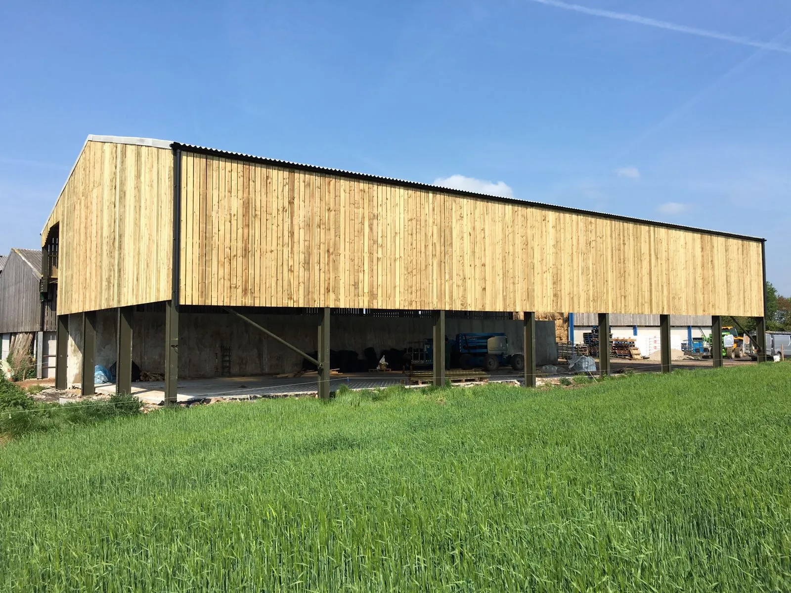 Timber-clad open-sided building raised on steel stanchions above a field of green grass