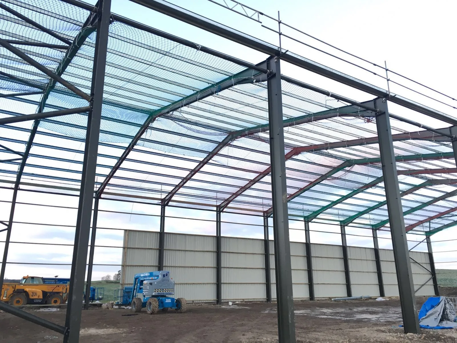 Interior view up into a steel frame, showing rafters, purlins and bracing against blue sky