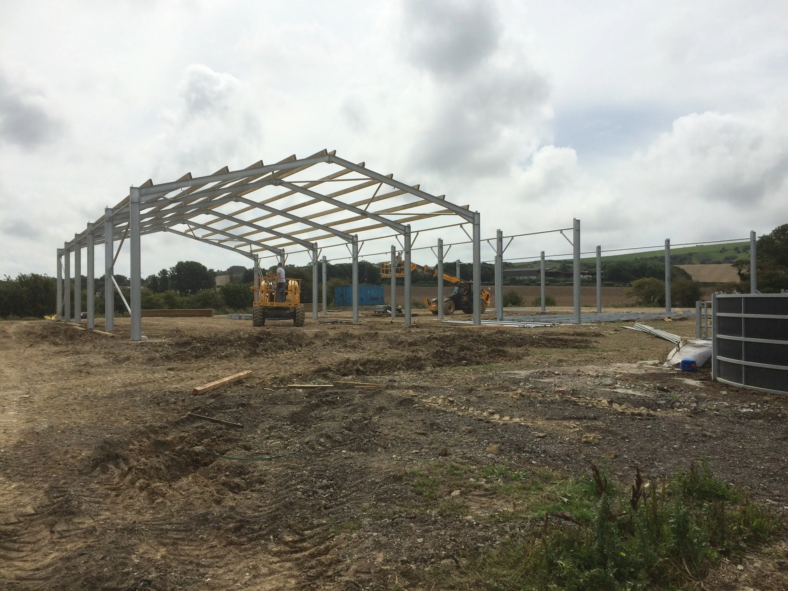 Steel portal frame under erection for an agricultural building, with telehandler on site