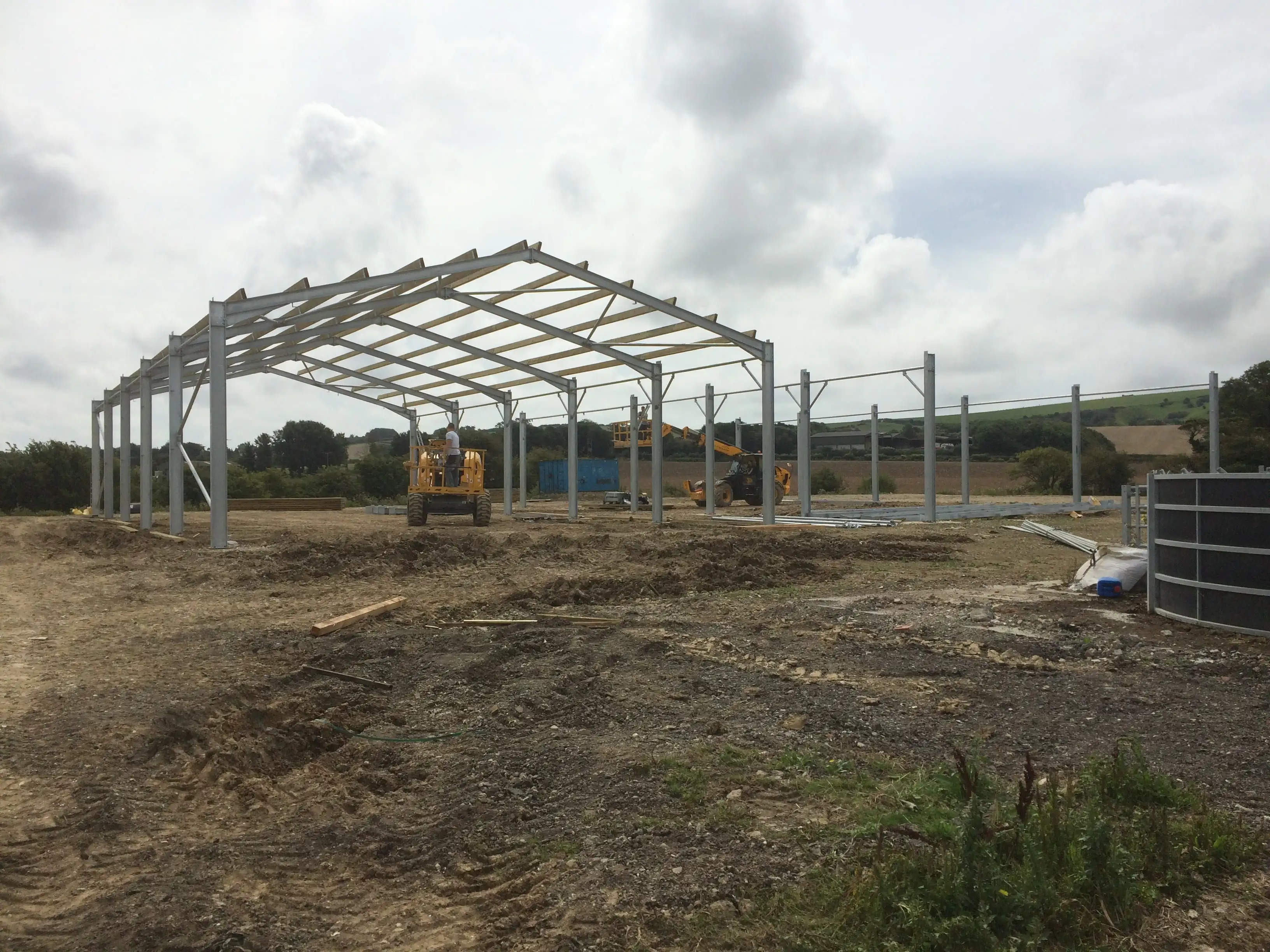 Steel portal frame partly erected for a new agricultural building, with a telehandler alongside