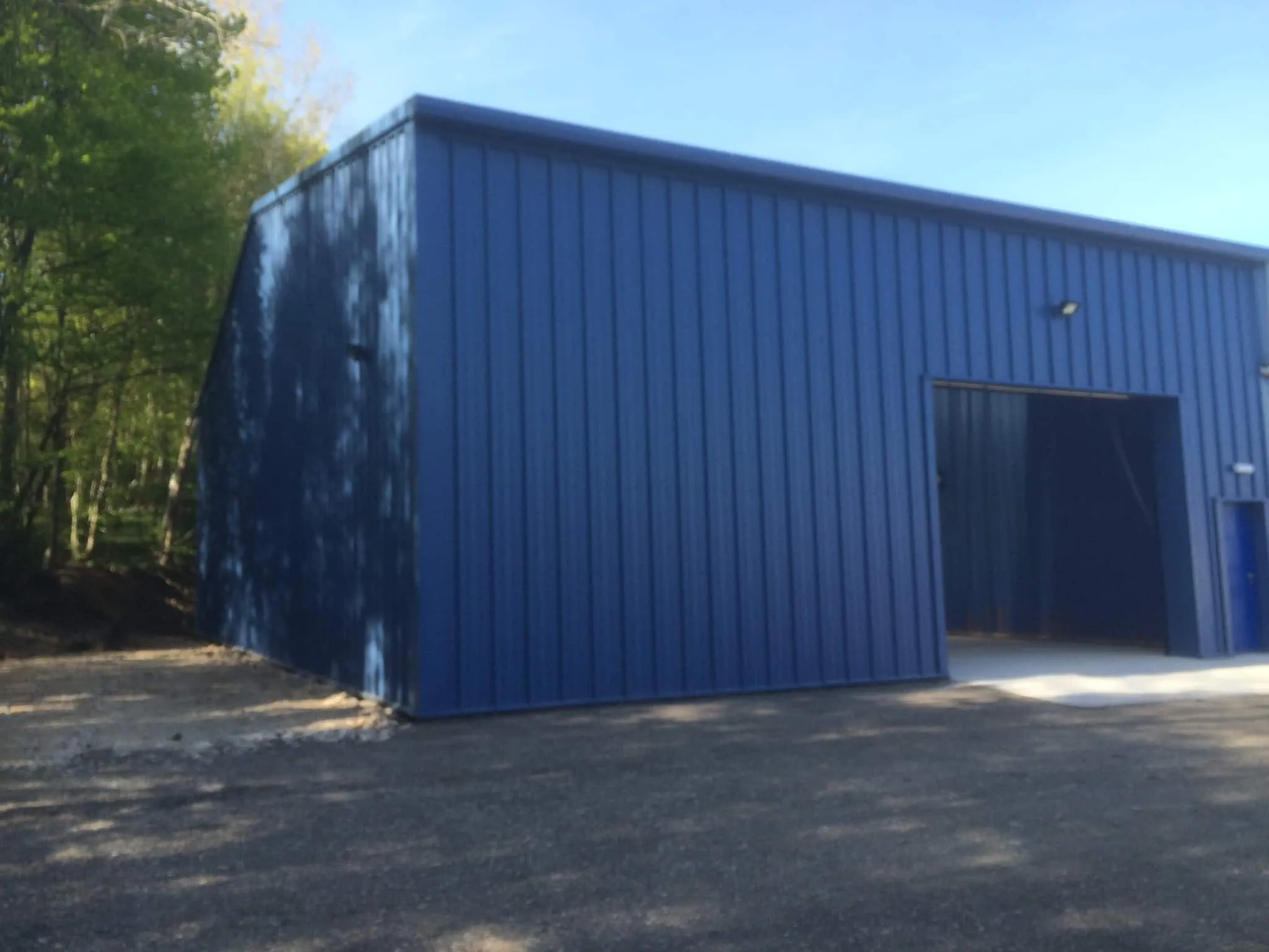 Blue profiled-sheet clad industrial building set against a backdrop of mature trees