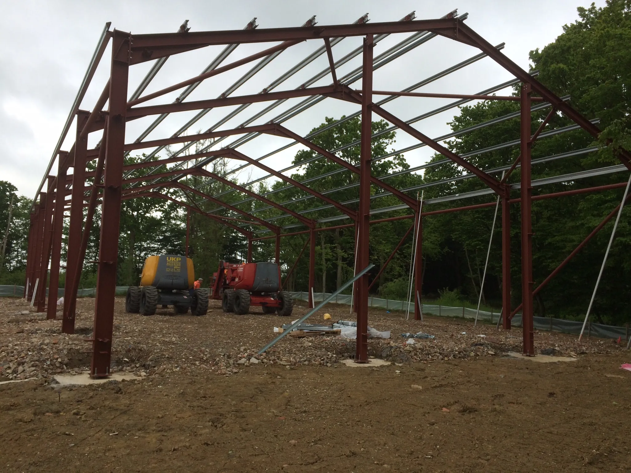 Erected steel frame with red-brown primer finish, telehandlers working beneath the open structure