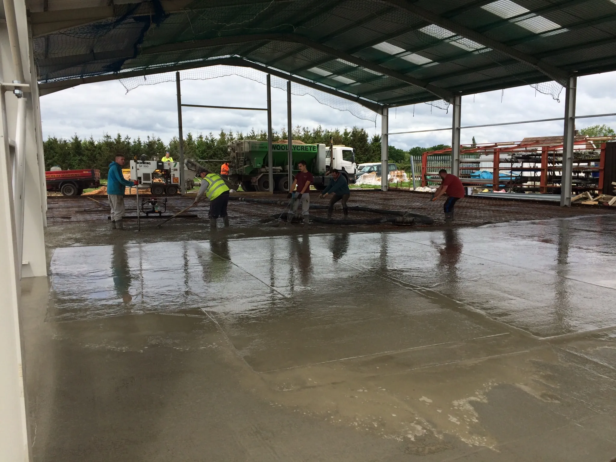 Large freshly poured concrete floor being worked by a team inside a steel-framed building