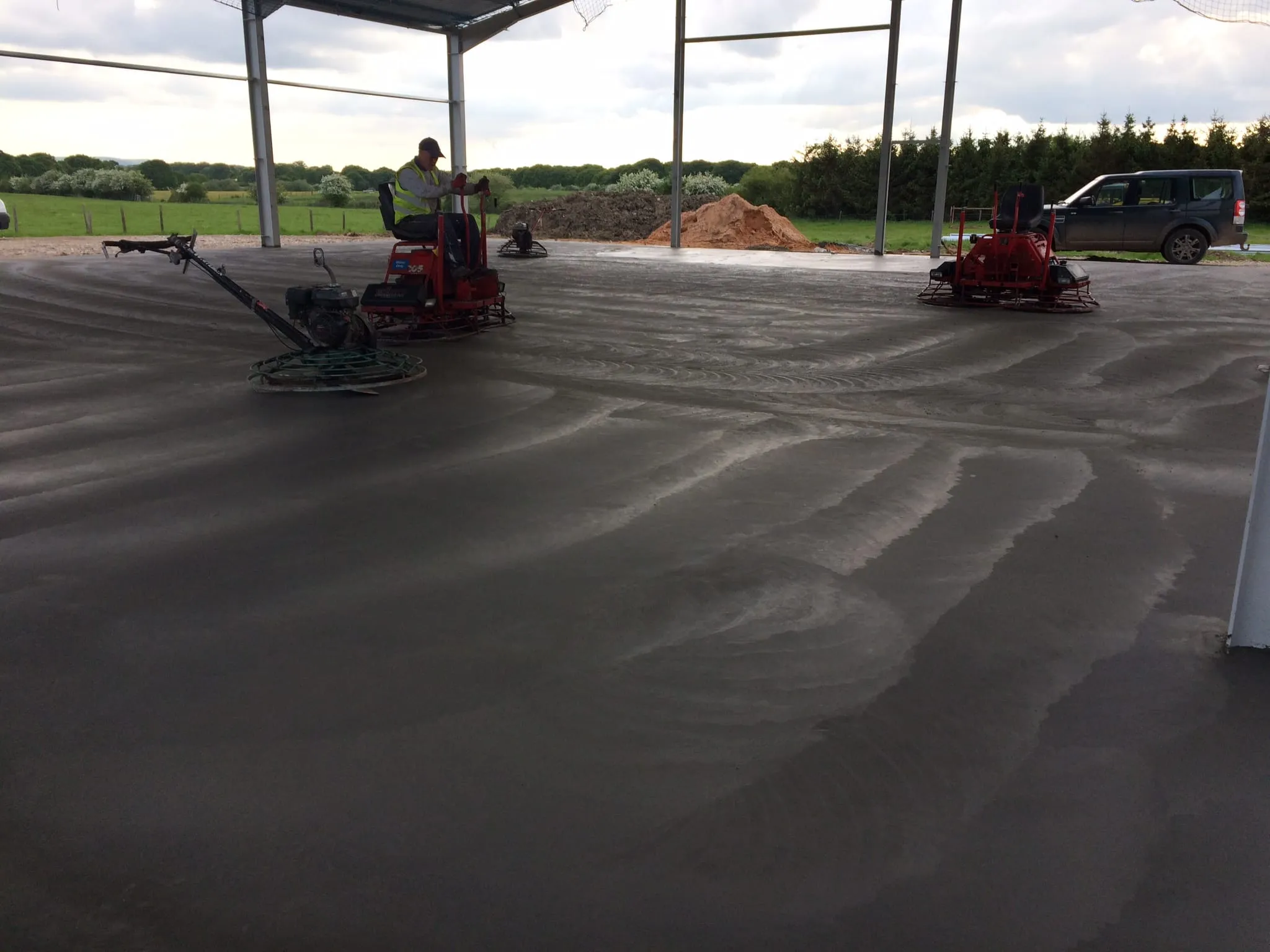 Two ride-on power floats working across a dark, freshly poured concrete slab