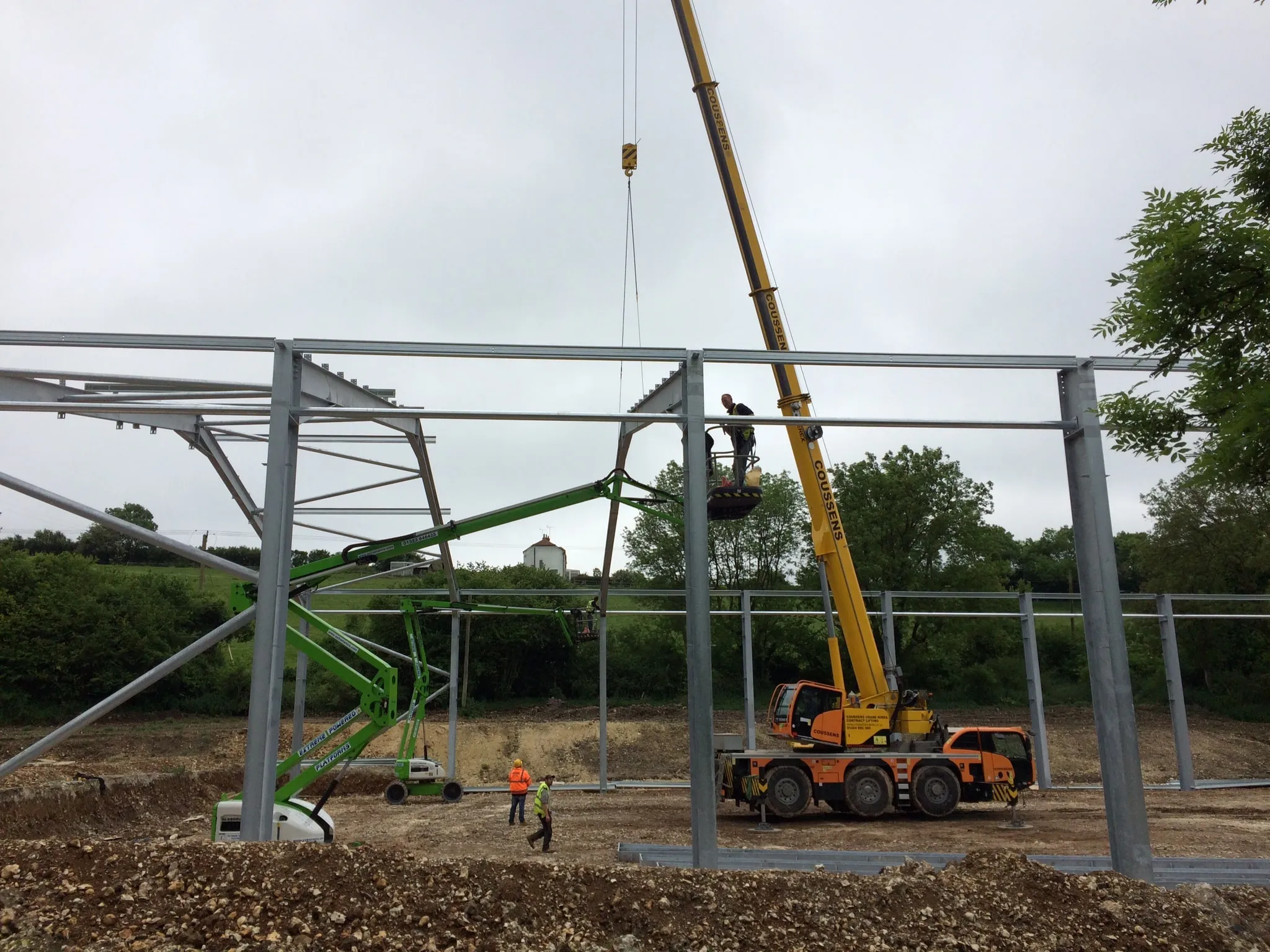 Mobile crane and cherry picker lifting steel rafters into position on a partly erected frame