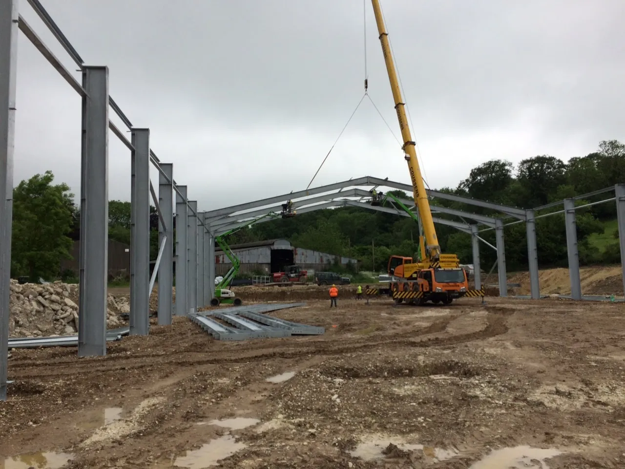 Steel frame under erection with a mobile crane alongside and rolling downland in the background