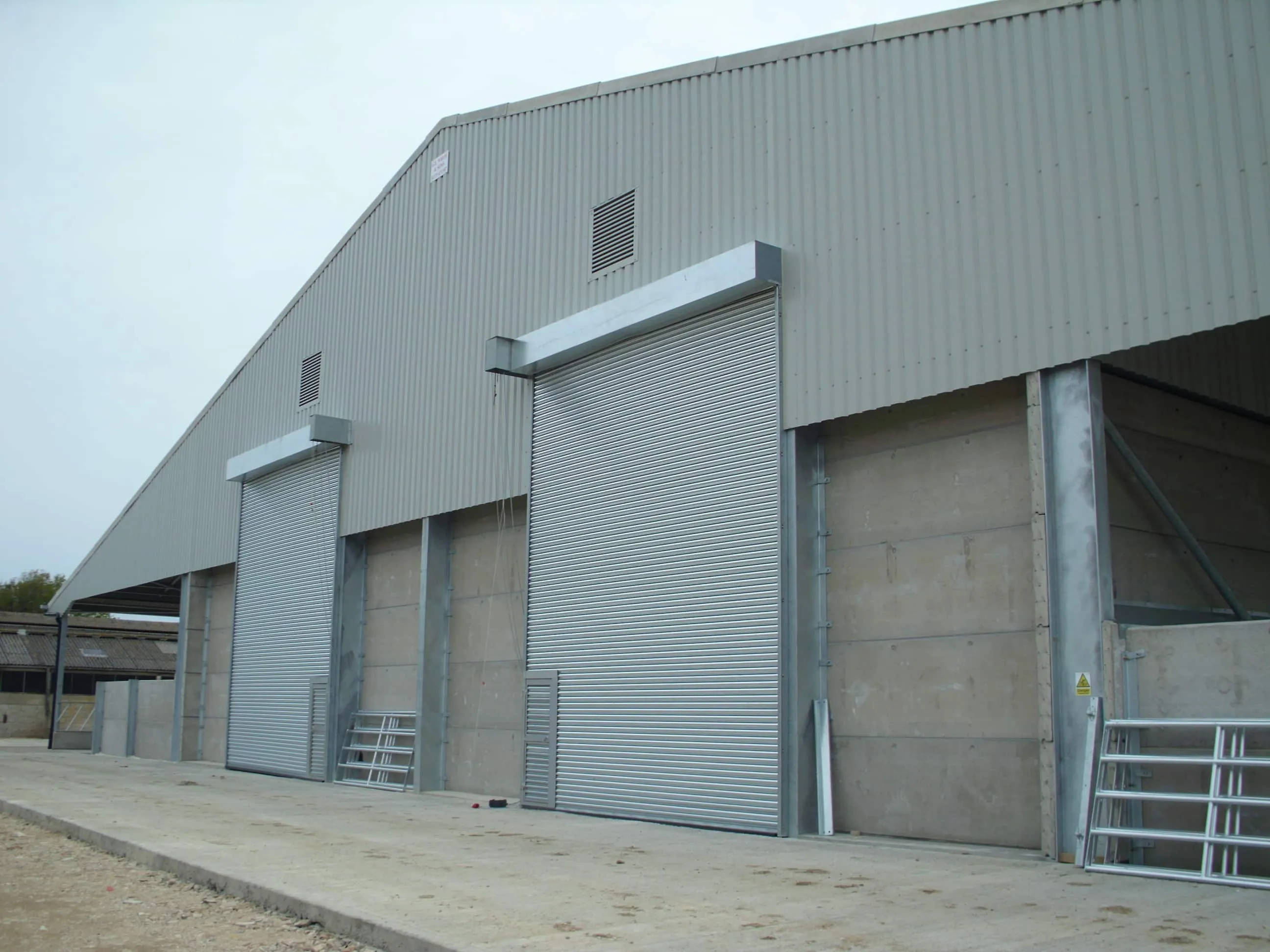 Grey clad industrial building with tall roller shutter doors and concrete panel walls