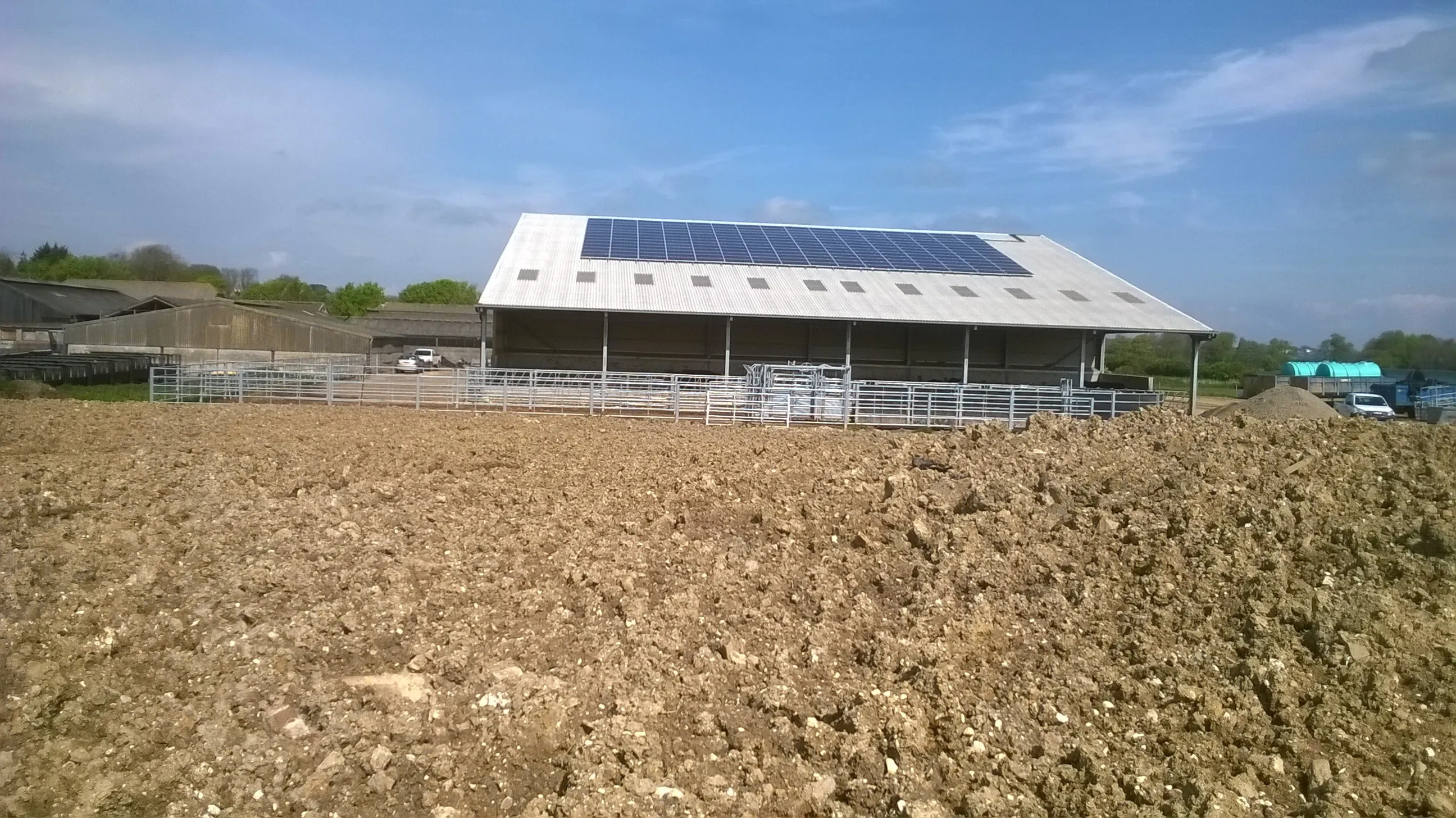 Agricultural building with a full array of solar panels across its south-facing roof slope, livestock pens in the foreground