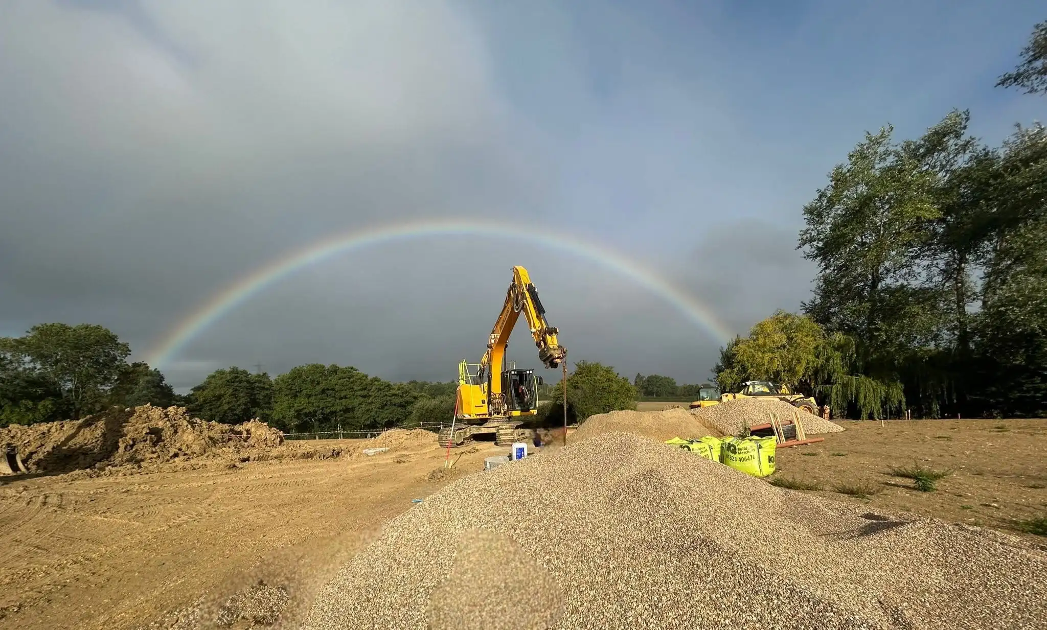 Woollard excavator working on a prepared earthworks site beneath a rainbow