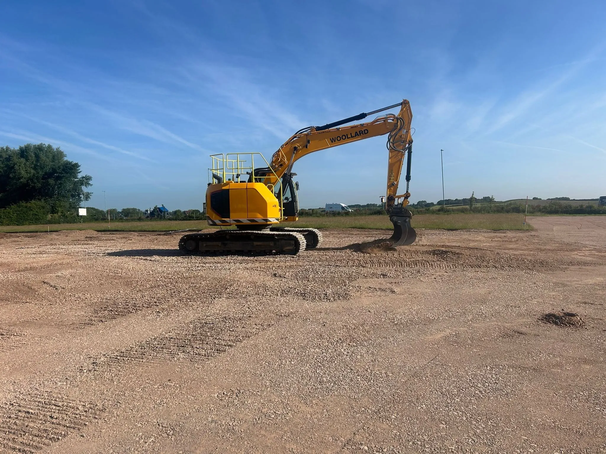 Woollard tracked excavator grading a large prepared platform under a clear blue sky