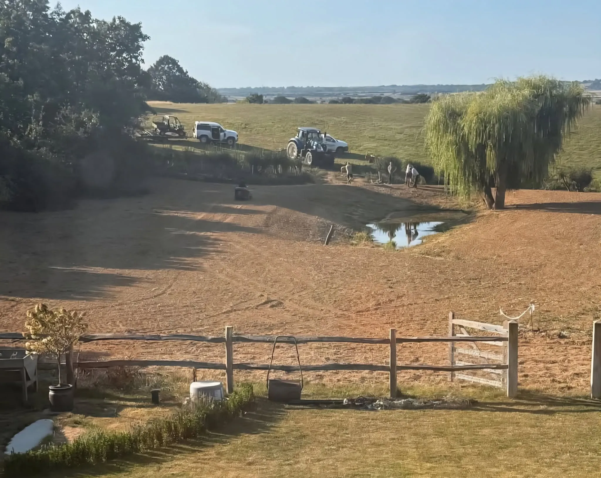 Landscaped pond with exposed banks, workers and site vehicles around the water edge
