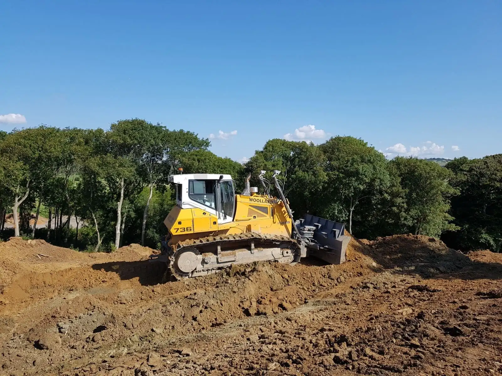 Woollard bulldozer grading earth on a hillside site under clear skies