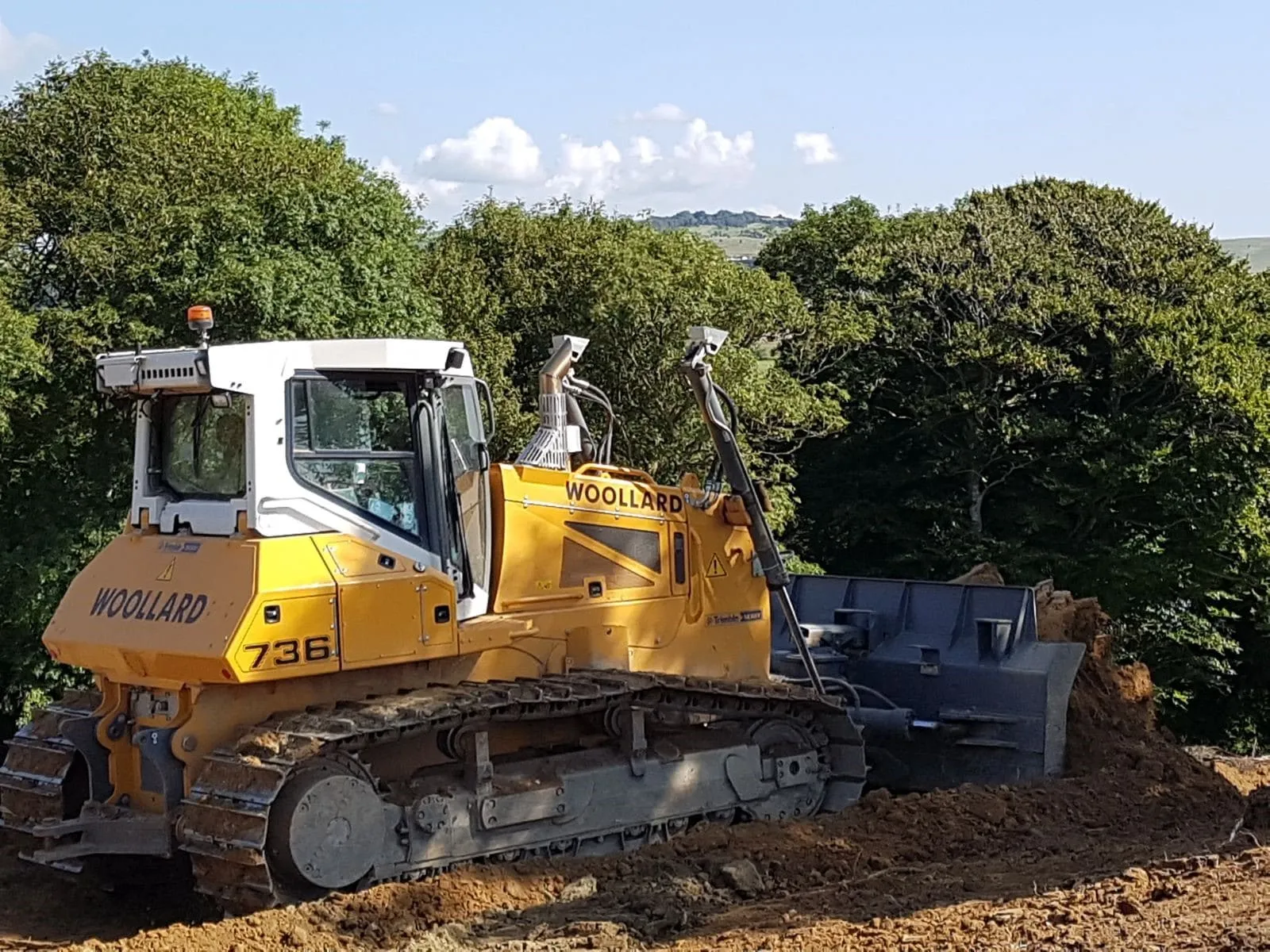 Close view of a Woollard-liveried bulldozer with its blade raised on freshly worked ground
